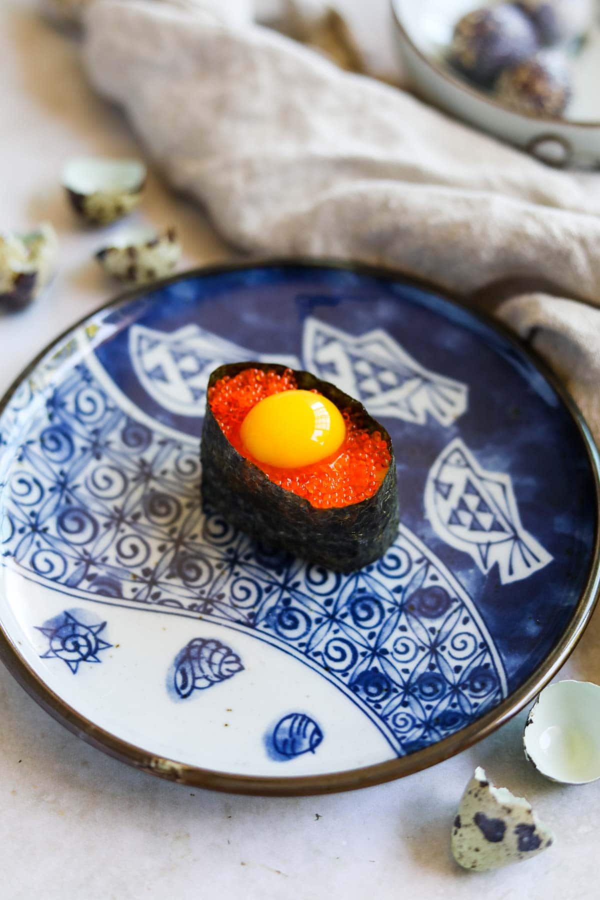 Tobiko quail egg gunkan sushi on a blue Japanese ceramic plate.