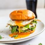 Fried egg cheeseburger with yolky egg, arugula, and grilled onions on a plate.