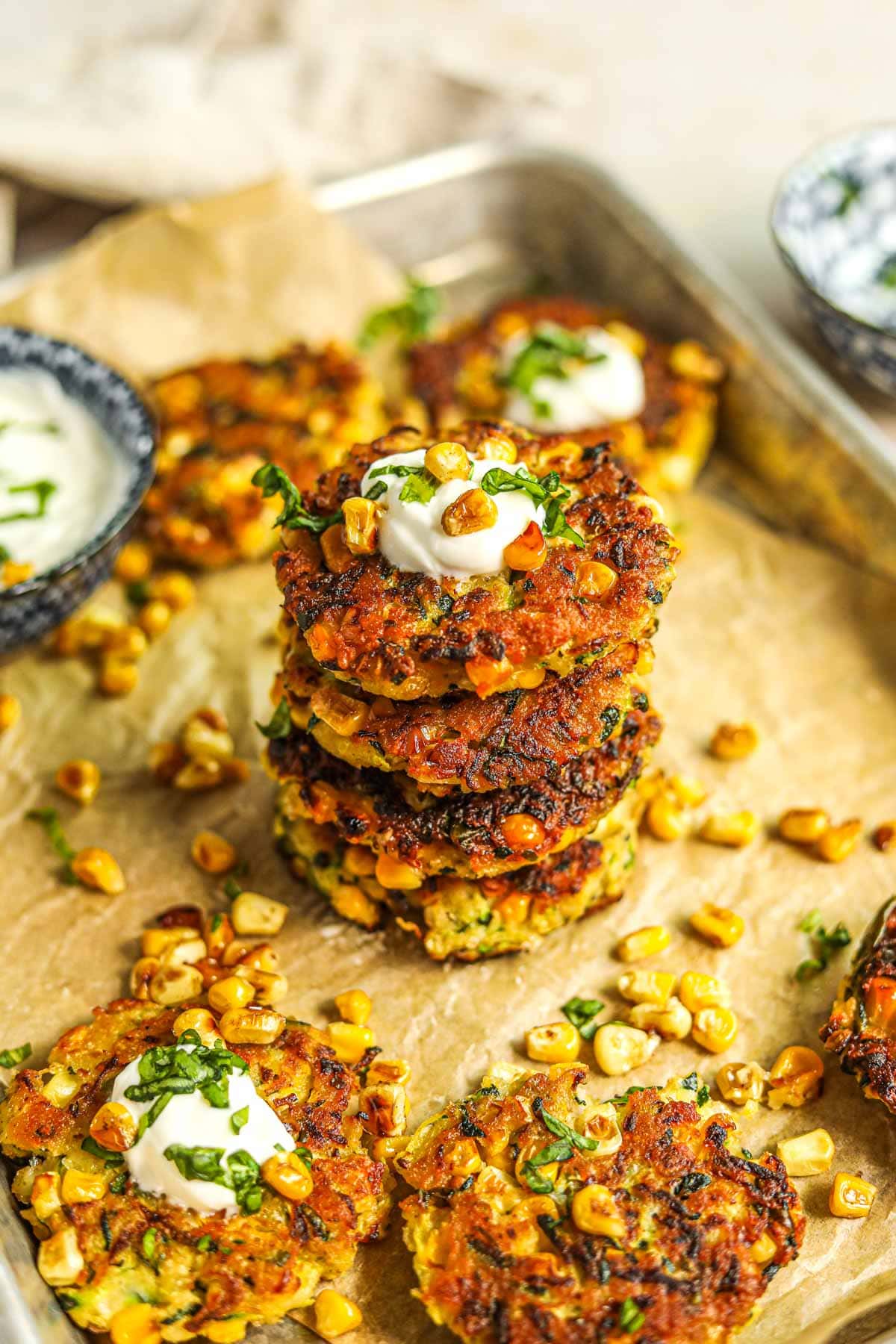 Healthy corn and zucchini fritter stacked and topped with greek yogurt, roasted corn, and basil.