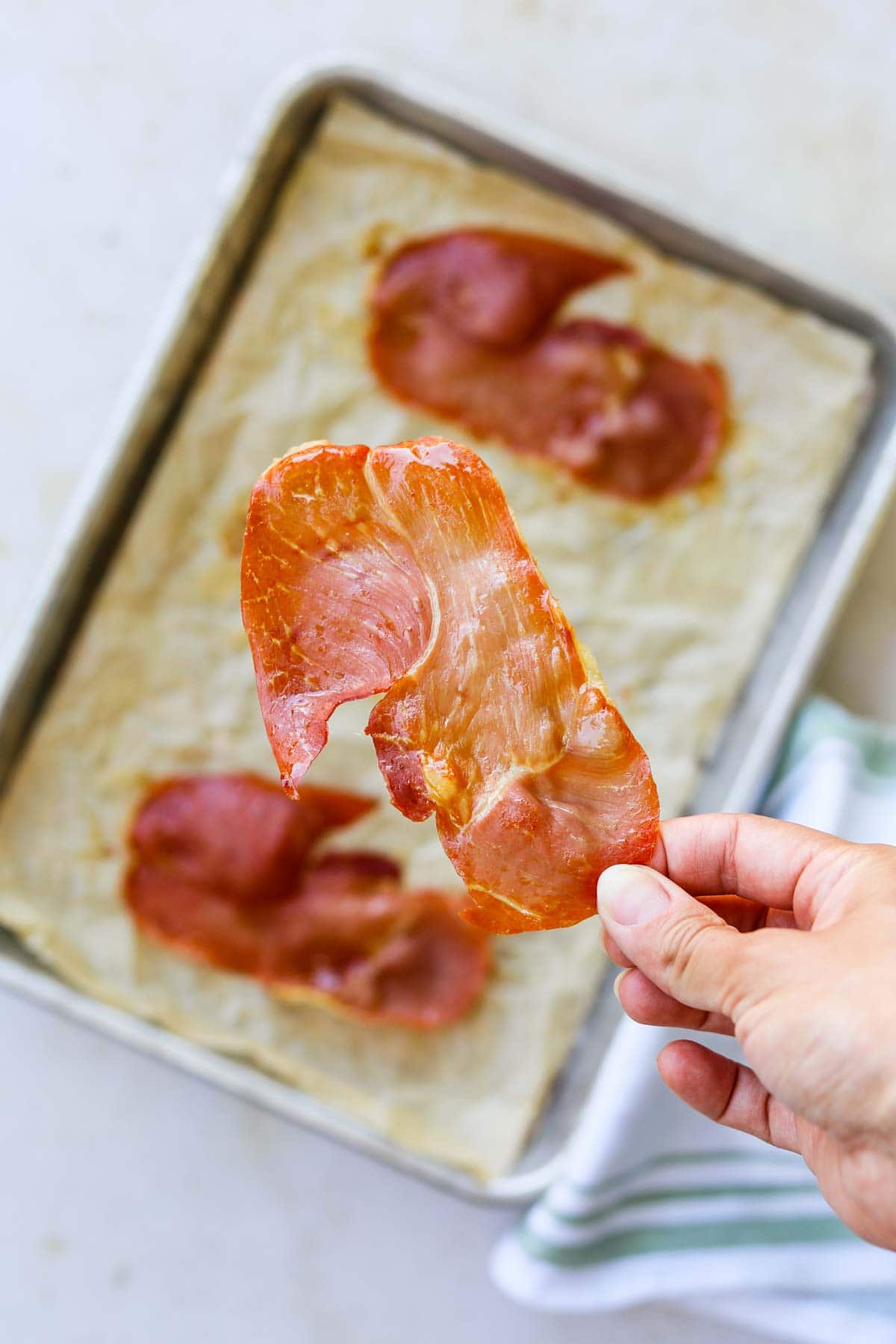 Hand holding a piece of oven-roasted crispy prosciutto.