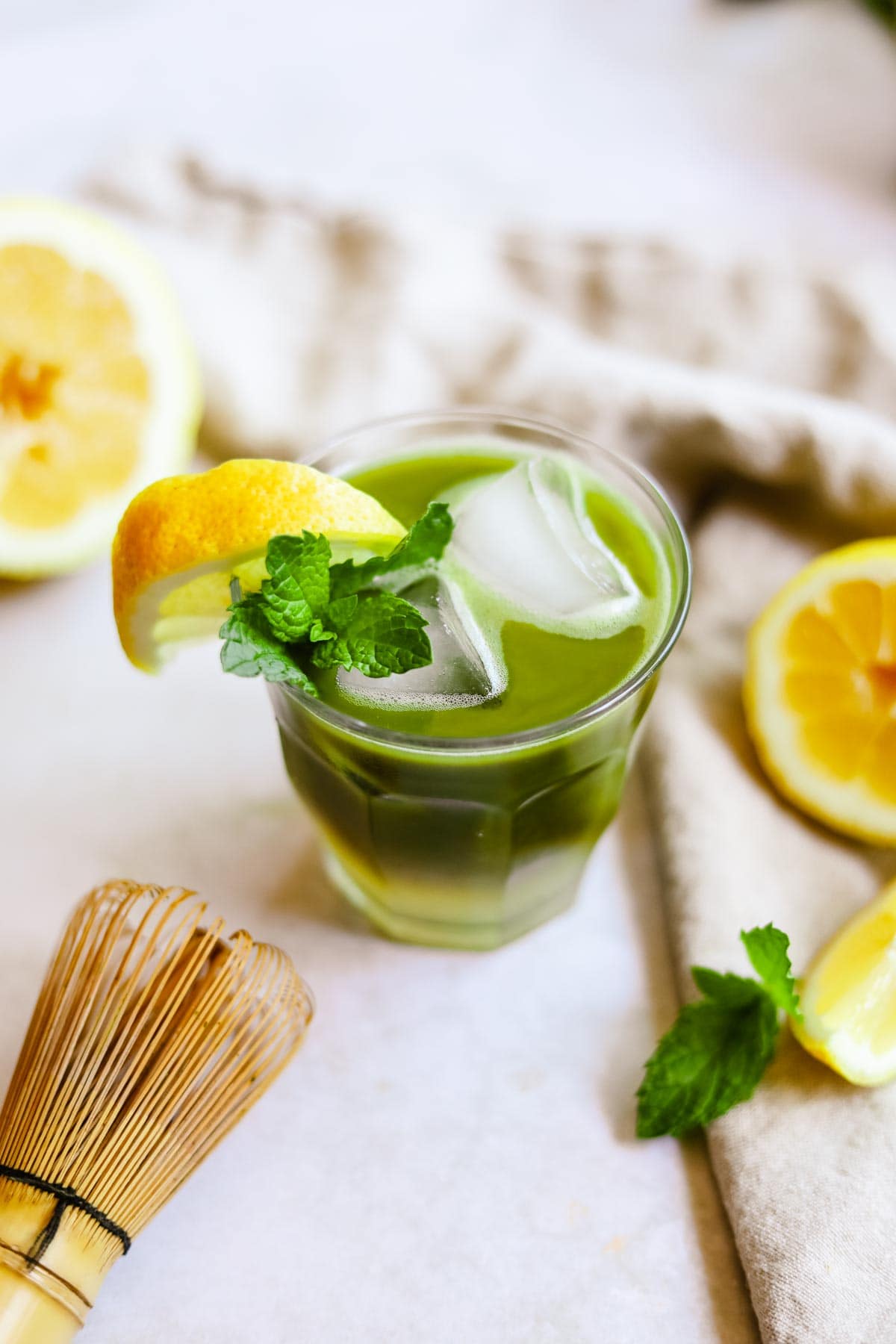 Green tea matcha lemonade in a glass with a lemon wedge and sprig of mint.