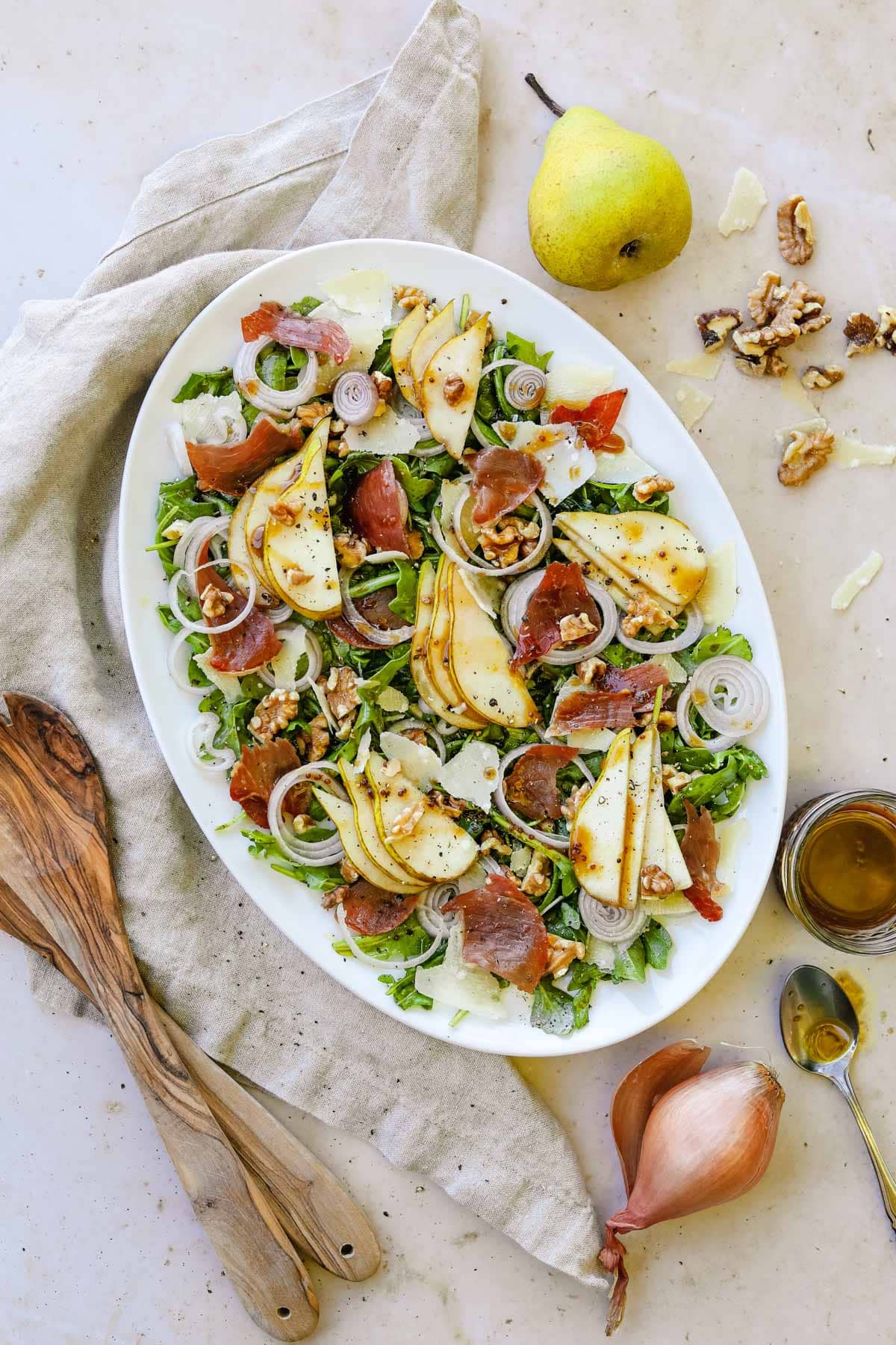 Pear and prosciutto rocket salad on a serving platter with sliced pears, crispy prosciutto, shallots, walnuts, arugula, and a maple balsamic vinaigrette vinaigrette.