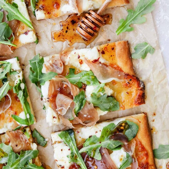 Prosciutto ricotta pizza with arugula and hot honey on parchment paper wit honey dripper.