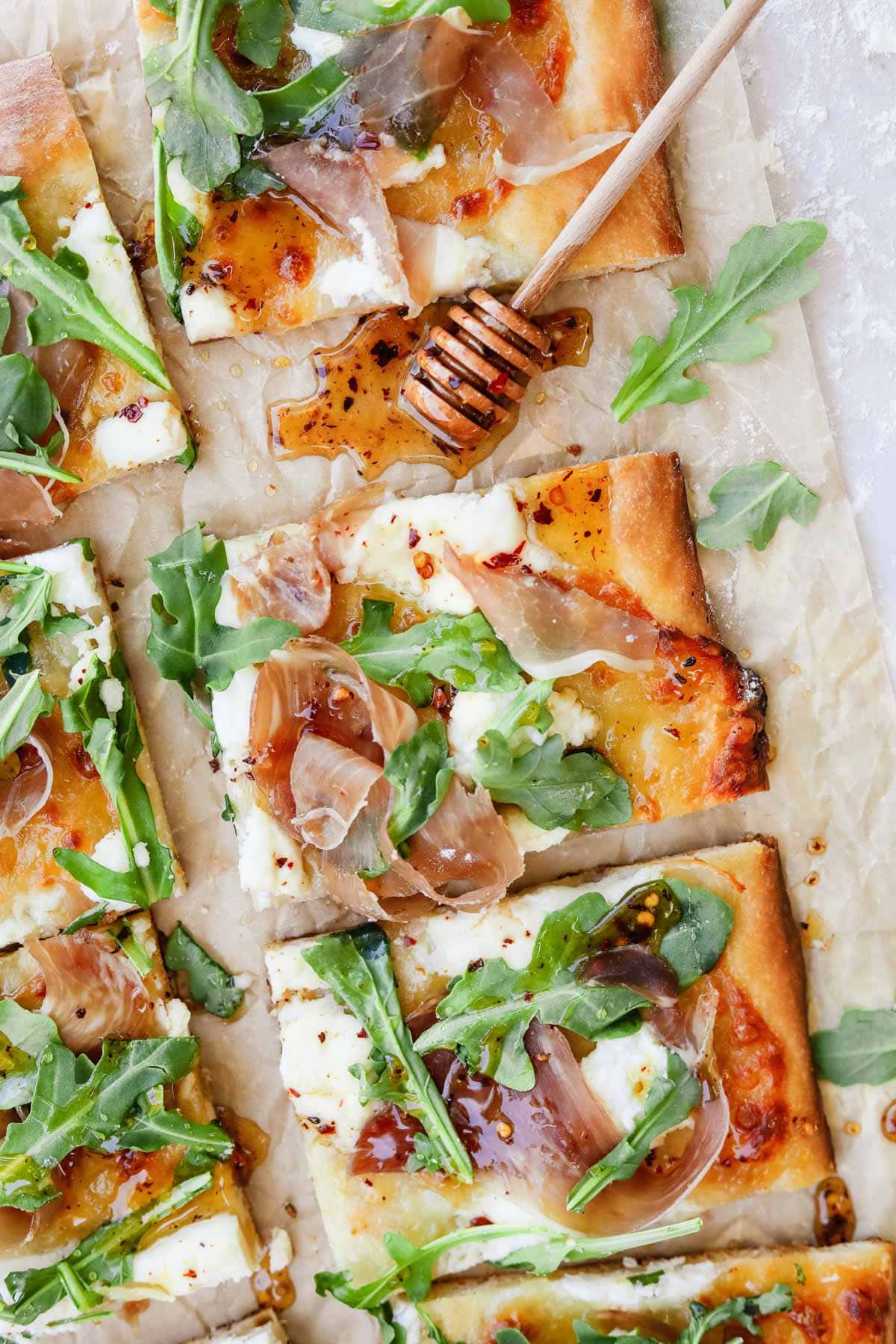 Prosciutto ricotta pizza with arugula and hot honey on parchment paper.