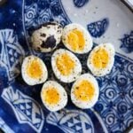 Peeled soft-boiled quail eggs cut in half on a plate with one whole, uncooked quail egg for comparison.
