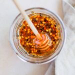 Spicy hot honey sauce in a jar with honey dripper overhead.