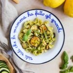 Veggie pesto pasta in a bowl topped with zucchini and asparagus with sliced zucchini, basil, parmigiano-reggiano, and lemons.