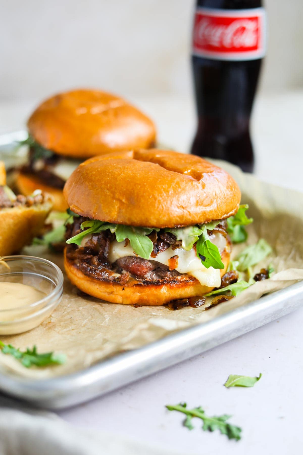 Wagyu beef cheeseburger with arugula, gruyere, grilled onions, and wasabi mayo on parchment paper with a Mexican coke.