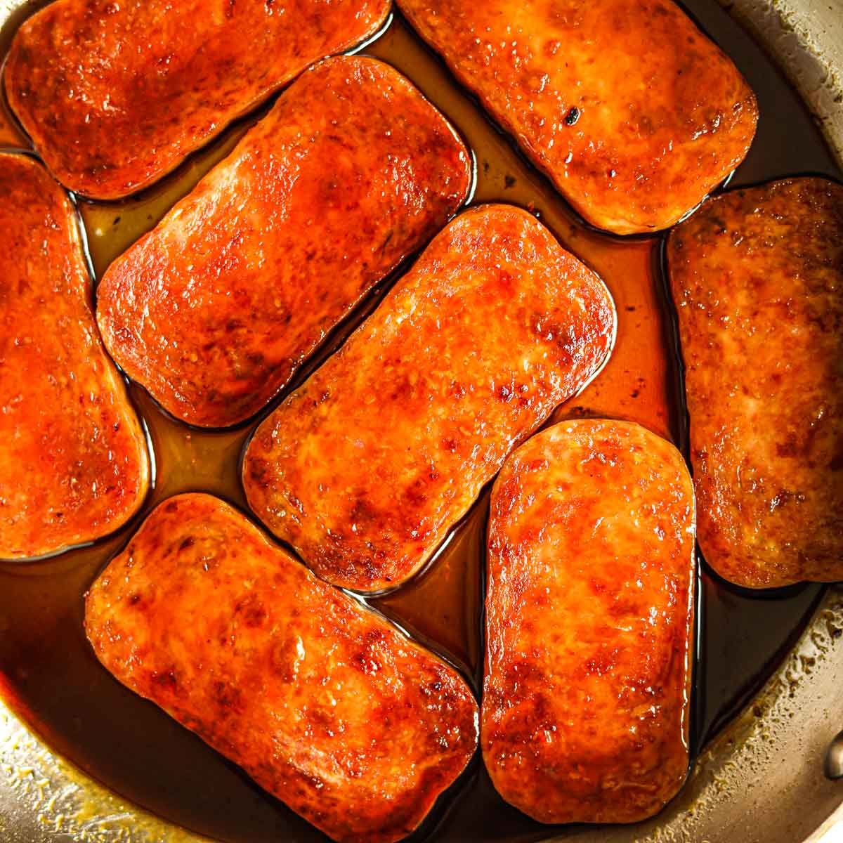Overhead shot of sliced Spam in a pan with homemade teriyaki sauce.