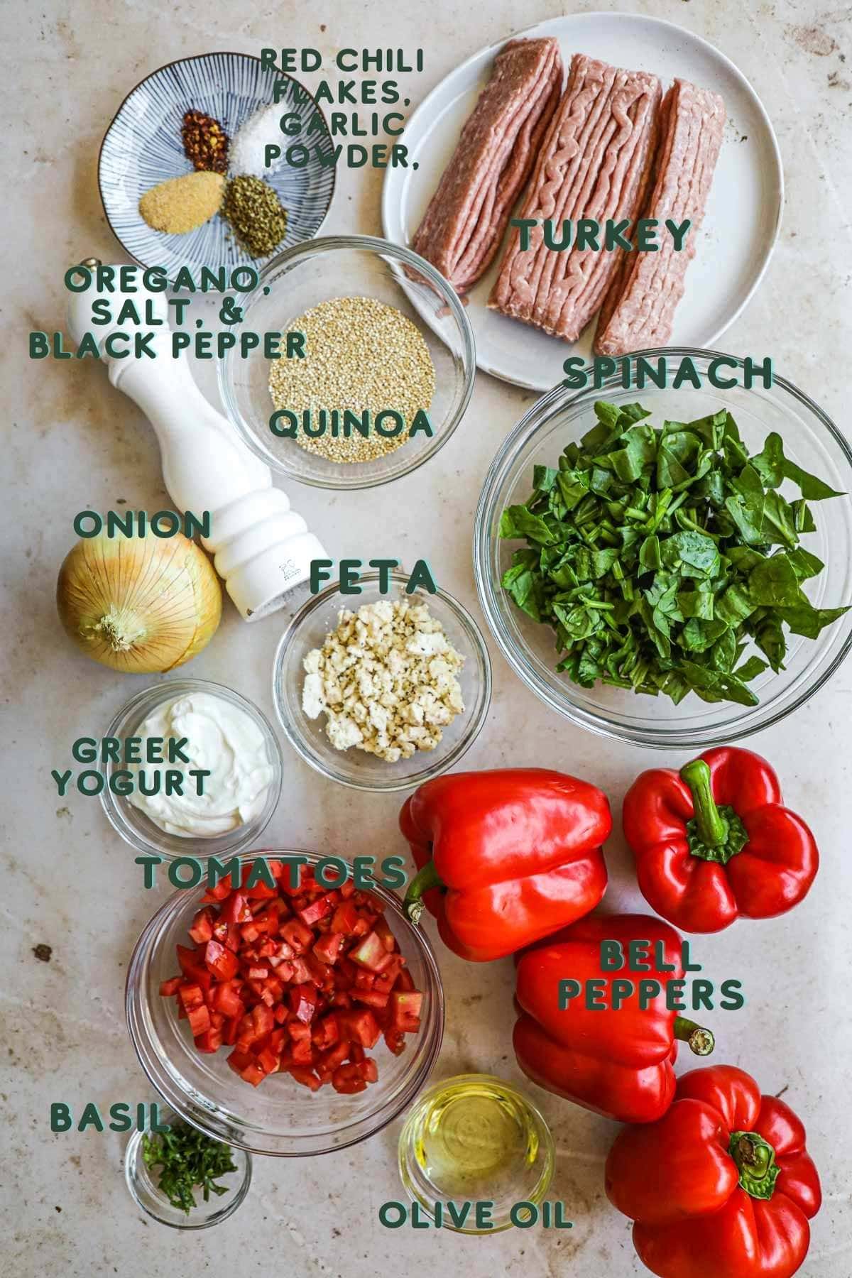 Ingredients to make quinoa and turkey bell peppers, including spices, tomatoes, feta, greek yogurt, spinach, basil, quinoa, and onion.
