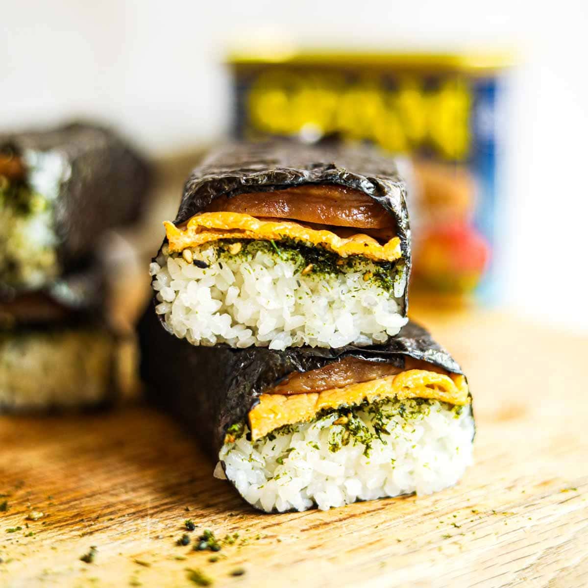 Spam musubi with egg and furikake stacked on a cutting board.