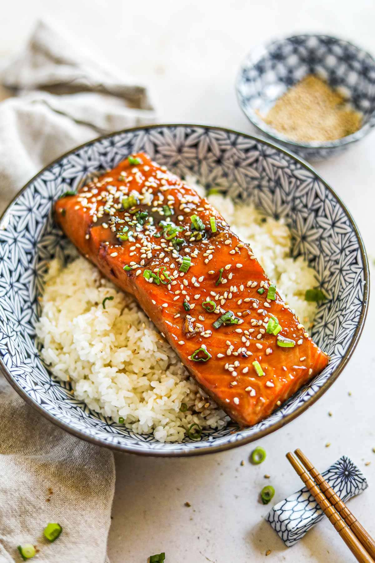 Teriyaki salmon rice bowl (donburi) in a blue Japanese porcelain bowl with chopsticks, garnished with sesame seeds and green onions.