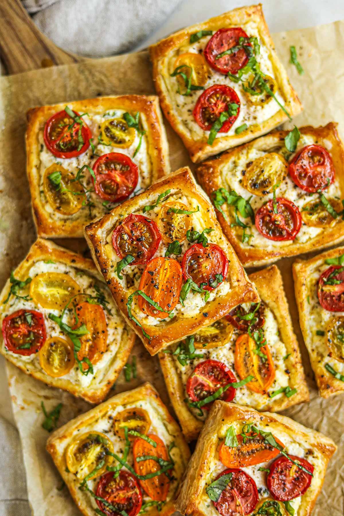 Tomato ricotta tartlets with heirloom tomatoes and fresh basil ribbons on a olive wood serving board.