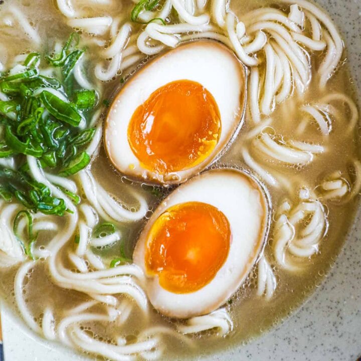 Ajitama (soft-boiled ramen egg) in a bowl of ramen noodle soup with scallions.