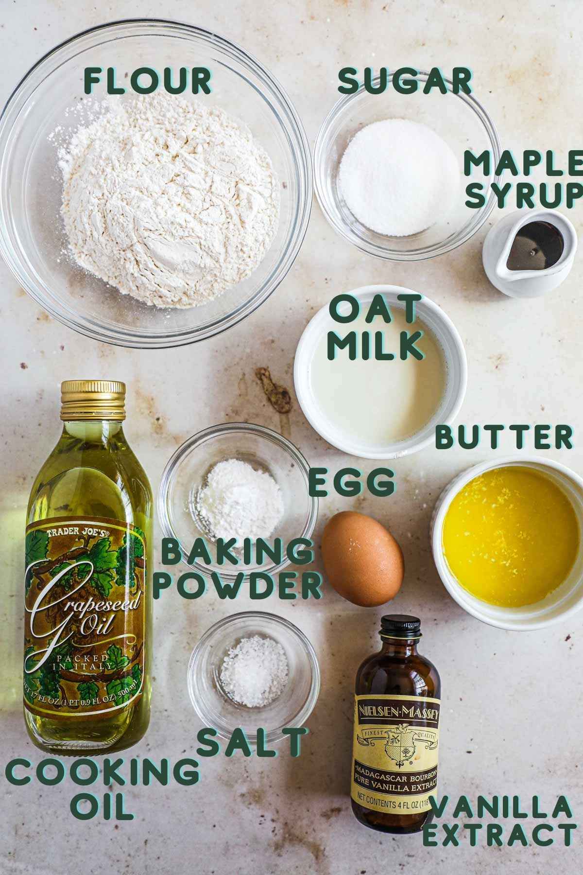 Ingredients to make fluffy oat milk pancakes, including flour, sugar, maple syrup, cooking oil, baking powder, salt, vanilla extract, egg, and butter.