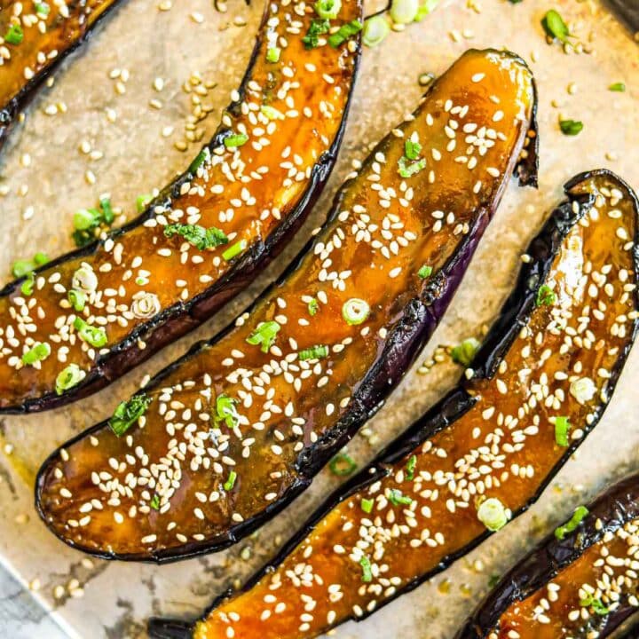 Miso-glazed Japanese eggplant with sesame seeds and sliced green onions on a baking sheet.