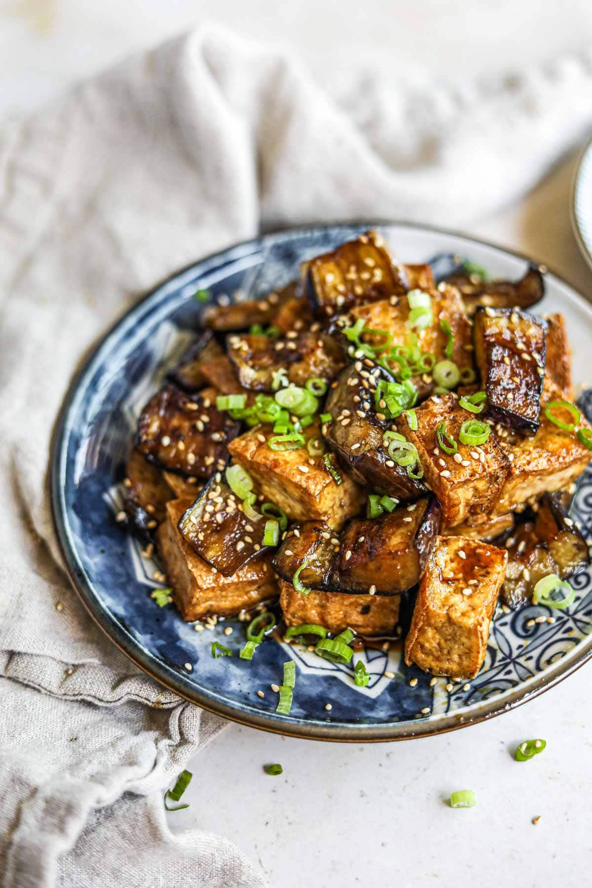 Teriyaki fried tofu and Japanese eggplant in a homemade gluten-free honey teriyaki sauce topped with sliced green onions and sesame seeds on a blue plate.