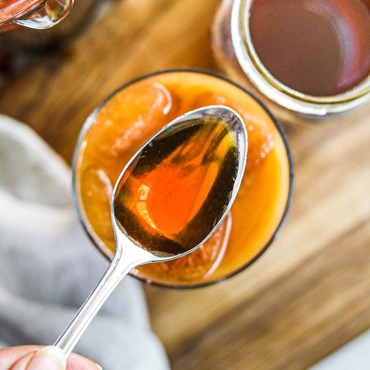 Homemade caramel syrup for coffee on a spoon with a glass of iced coffee.
