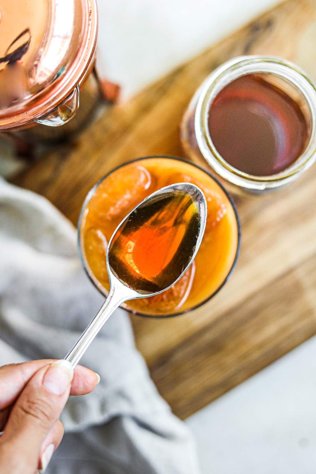 Homemade caramel syrup for coffee on a spoon with a glass of iced coffee.