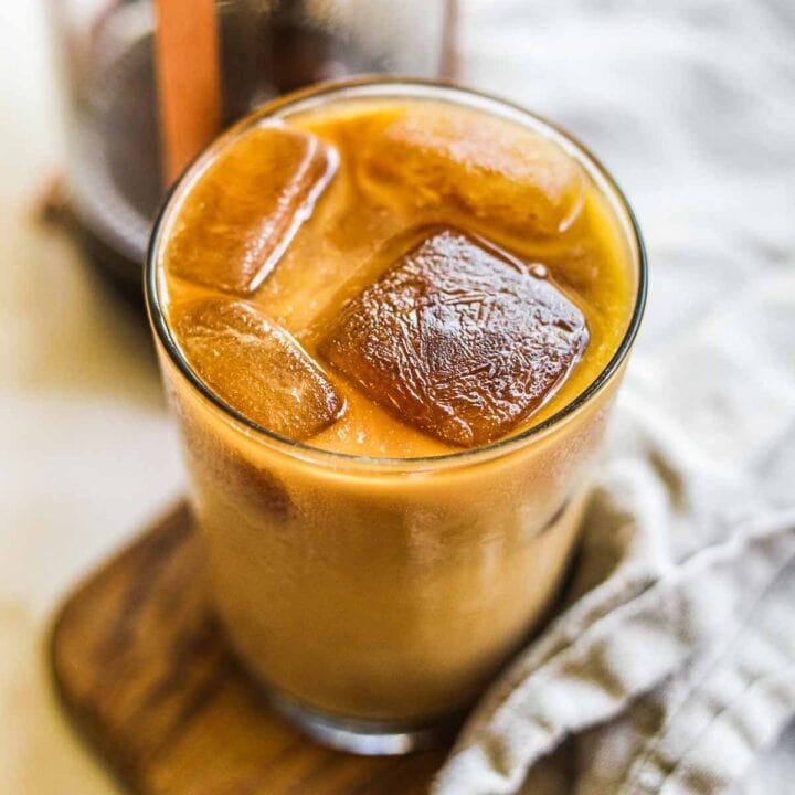 Homemade iced coffee in a glass with oat milk, coffee ice cubes, brewed coffee or espresso, and sweetener.