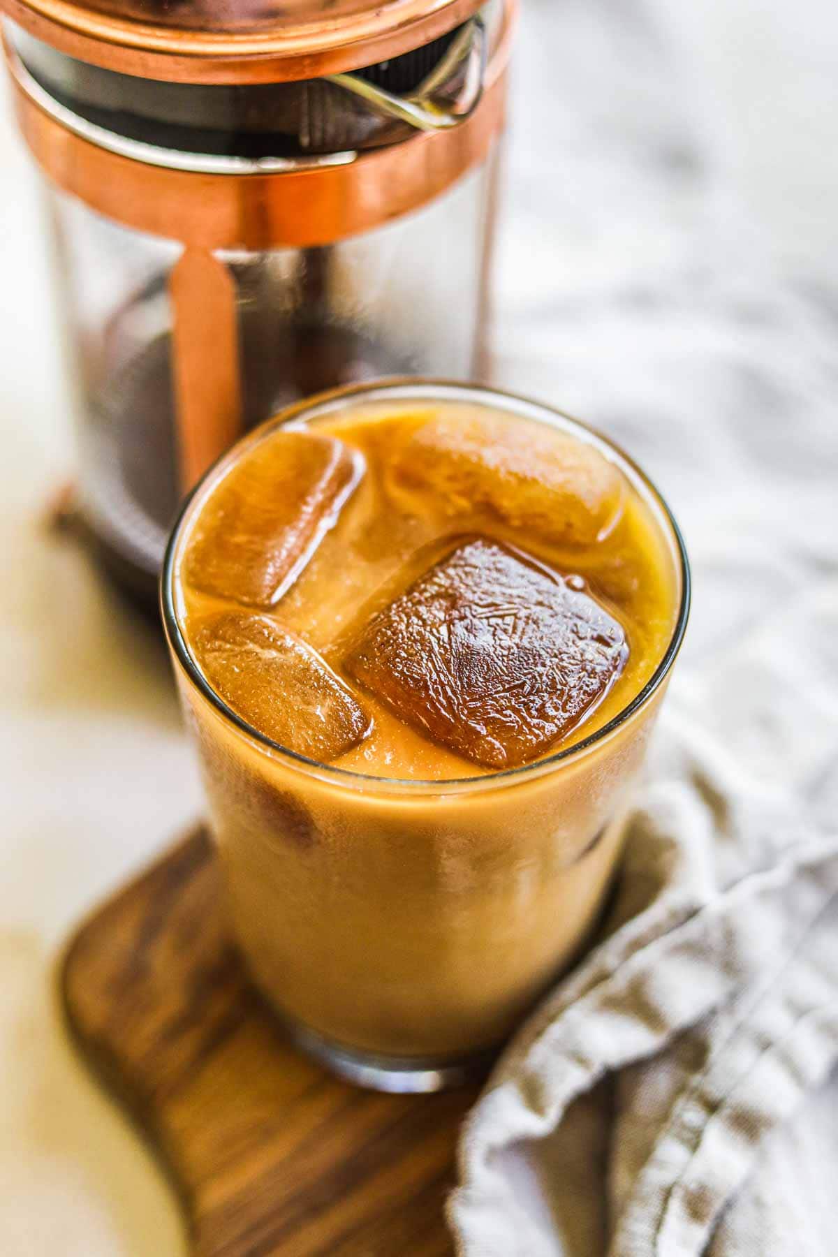 Homemade iced coffee in a glass with oat milk, coffee ice cubes, brewed coffee or espresso, and sweetener.