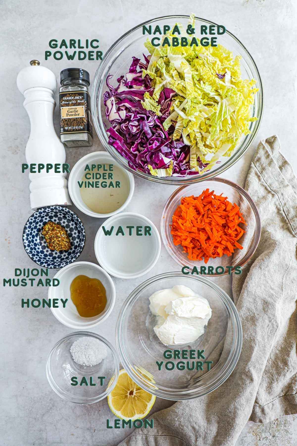 Ingredients to make a healthy Greek yogurt coleslaw recipe, including red cabbage, napa cabbage, carrots, Greek yogurt, honey, apple cider vinegar, water, garlic powder, dijon mustard, lemon juice, and kosher salt.