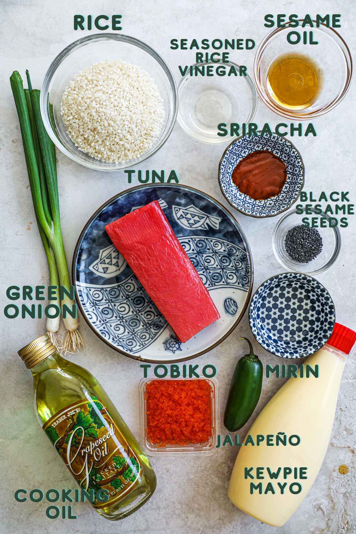 Ingredients to make spicy tuna with crispy rice, including kewpie mayo, Japanese rice, ahi, tobiko, green onions, sesame oil, black sesame seeds, sriracha, mirin, jalapeño, and seasoned rice vinegar.