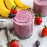 Purple blackberry strawberry banana smoothie in a glass garnished with fresh strawberries and blackberries.