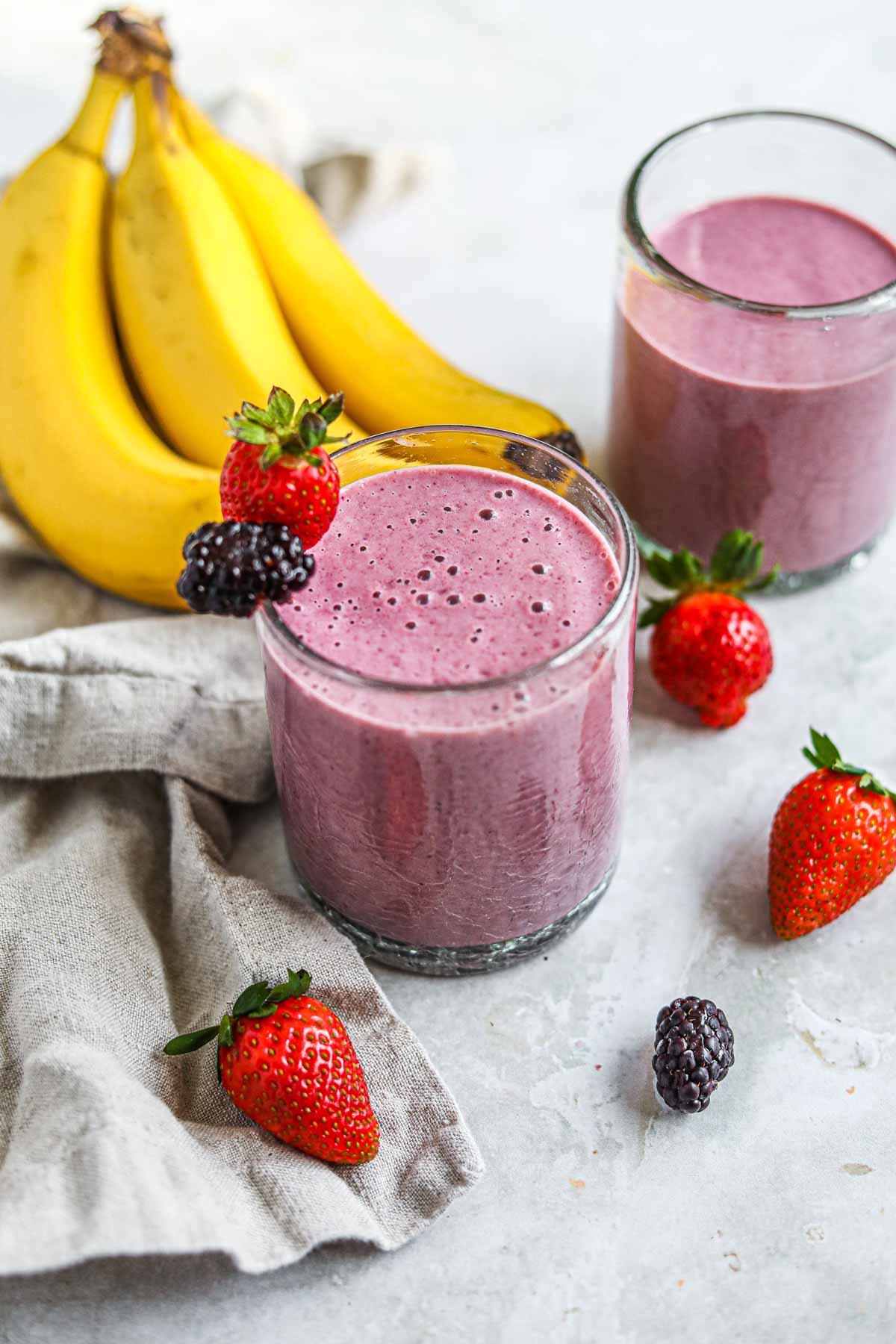 Purple blackberry strawberry banana smoothie in a glass garnished with fresh strawberries and blackberries.