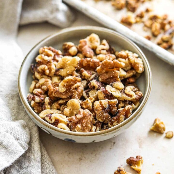 Roasted toasted walnuts in a serving bowl and on a baking sheet.