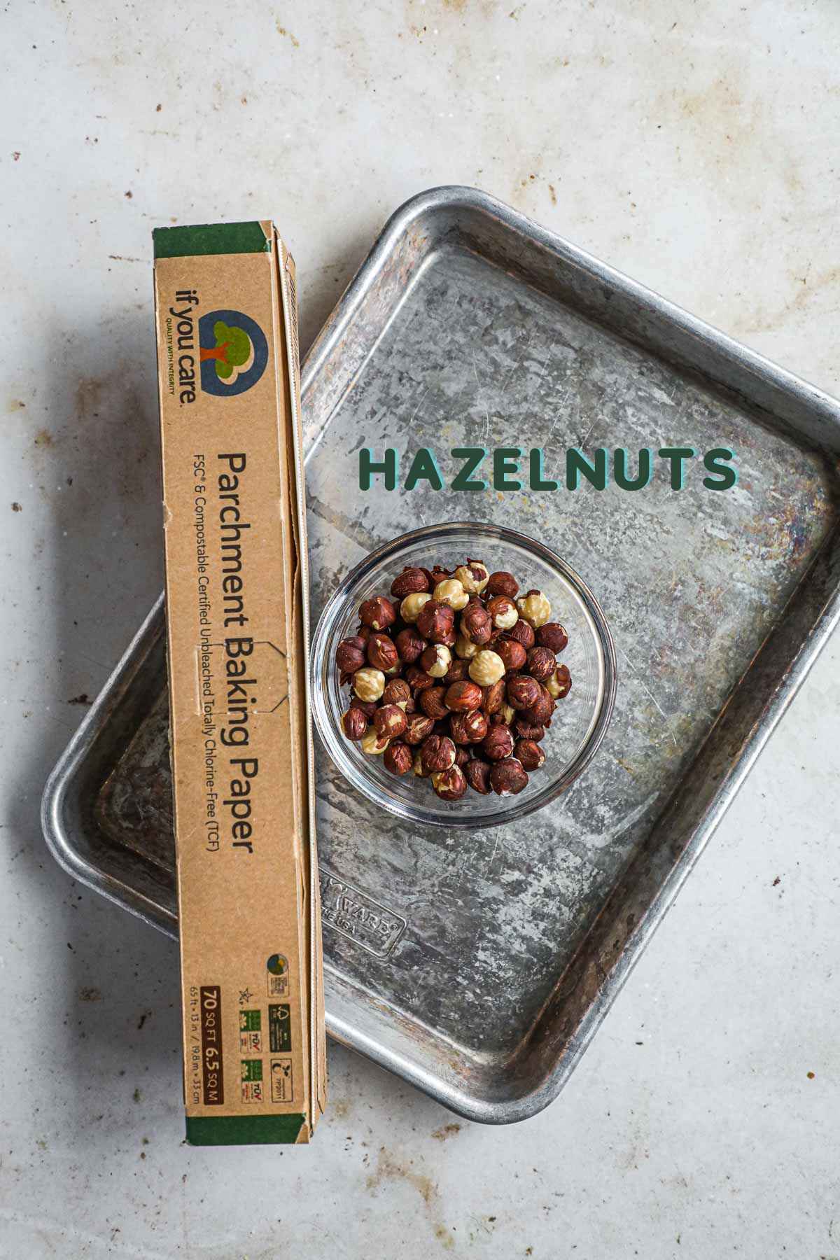 Ingredients to make roasted hazelnuts, including hazelnuts, parchment paper, and a sheet pan or a skillet.