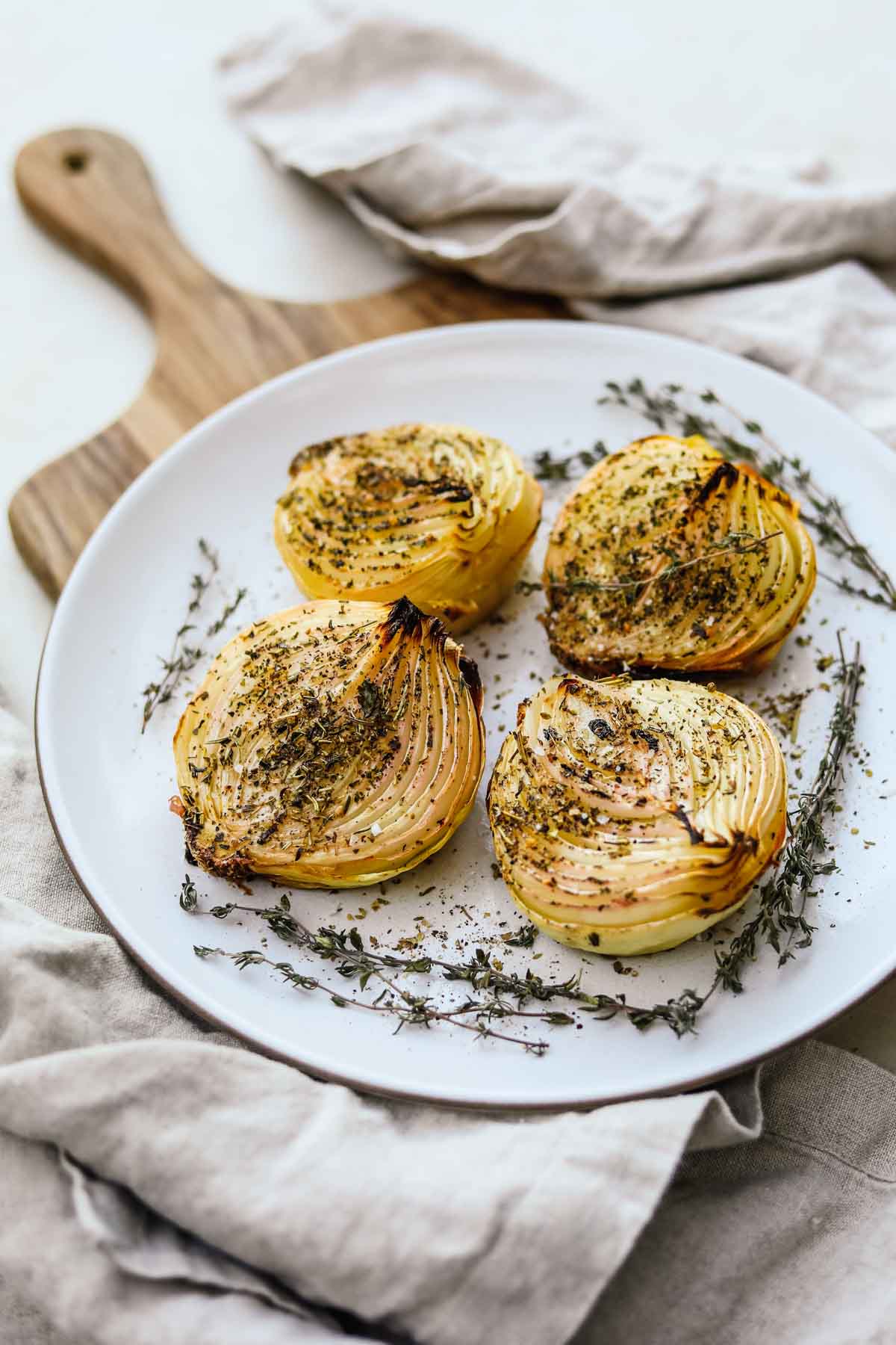 Oven roasted herb onions served on a platter with dried herbs and flaky sea salt.
