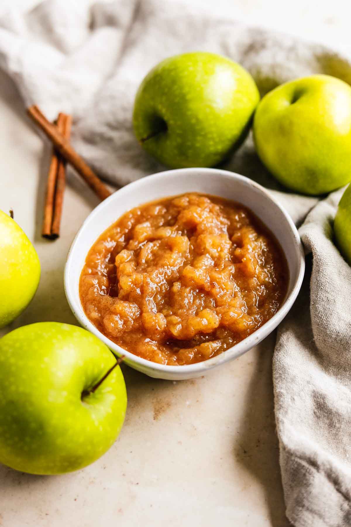 Sugar-free unsweetened apple sauce with cinnamon in a bowl with Granny Smith apples and cinnamon sticks.