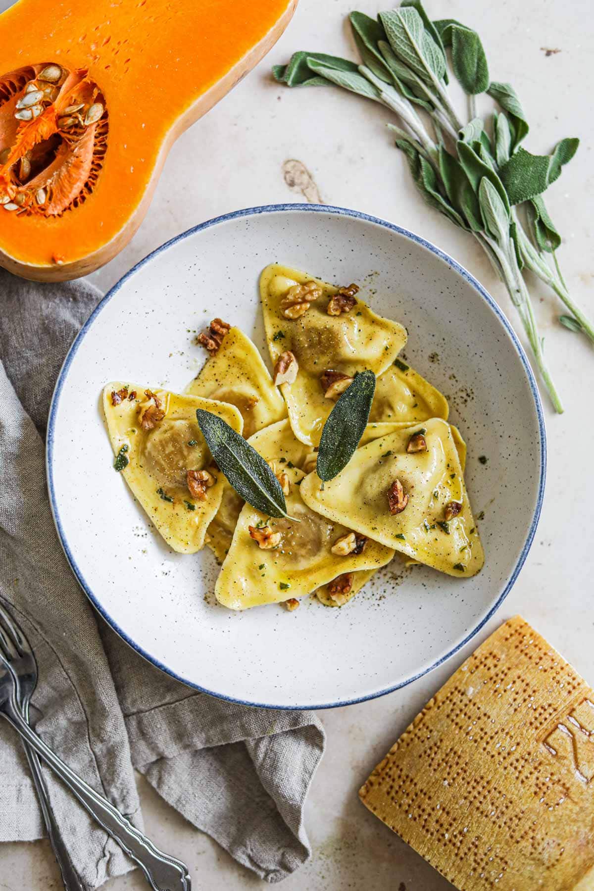 Trader Joe's triangle butternut squash ravioli in a browned butter olive oil sauce with crispy fried sage leaves and toasted walnuts in a bowl.