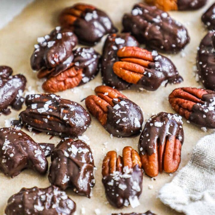 Homemade chocolate-covered pecans with flaky sea salt on a sheet of parchment paper.