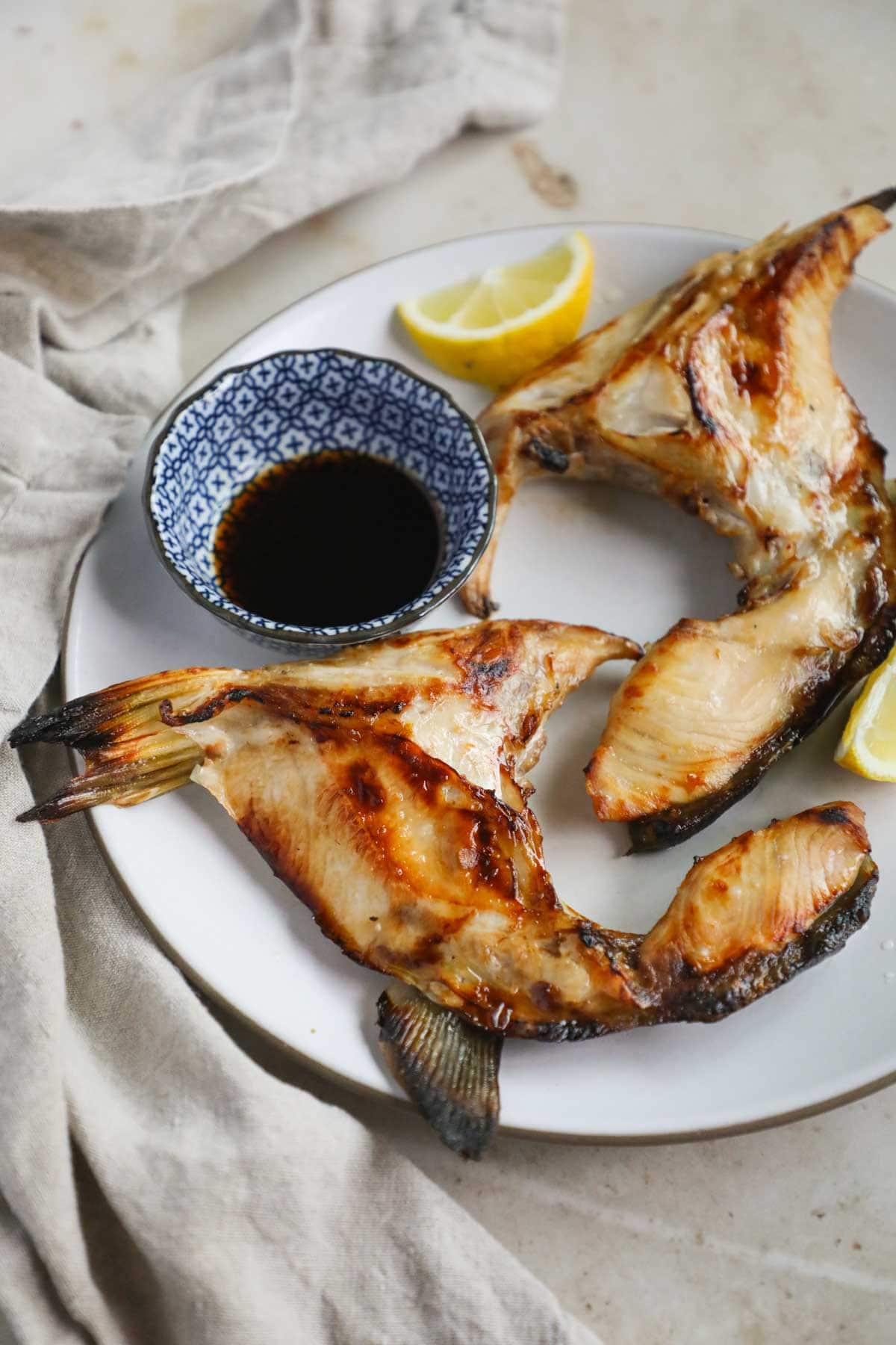 Broiled Japanese hamachi kama (yellowtail collar) with mirin, lemon juice, and soy sauce on a plate.
