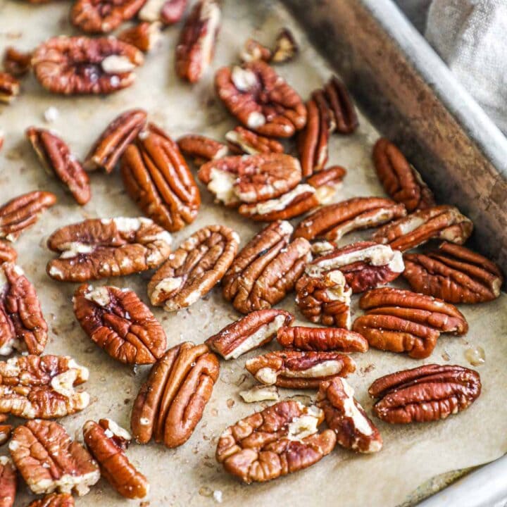 Oven toasted pecans on a parchment paper-lined sheet pan with sea salt and olive oil.