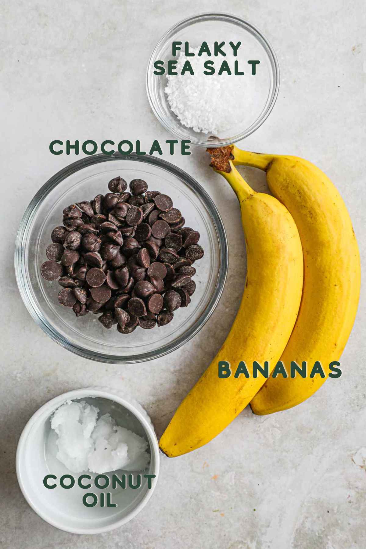 Ingredients to make chocolate-covered bananas, including chocolate, sliced bananas, coconut oil (optional), and flaky sea salt.