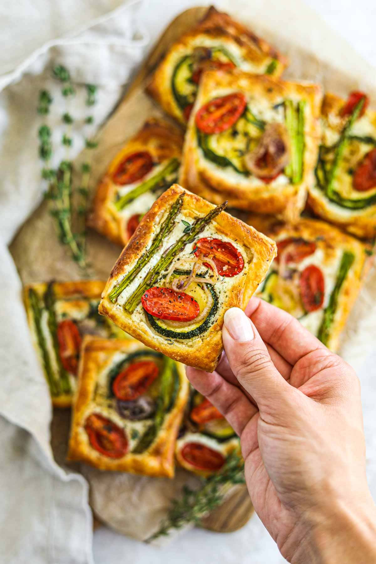 Photo of hand holding a goat cheese puff pastry vegetable tart.