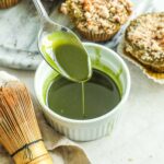 Spoon pouring matcha vanilla bean glaze for cakes, muffins, quick breads, and more in a white ceramic ramekin.