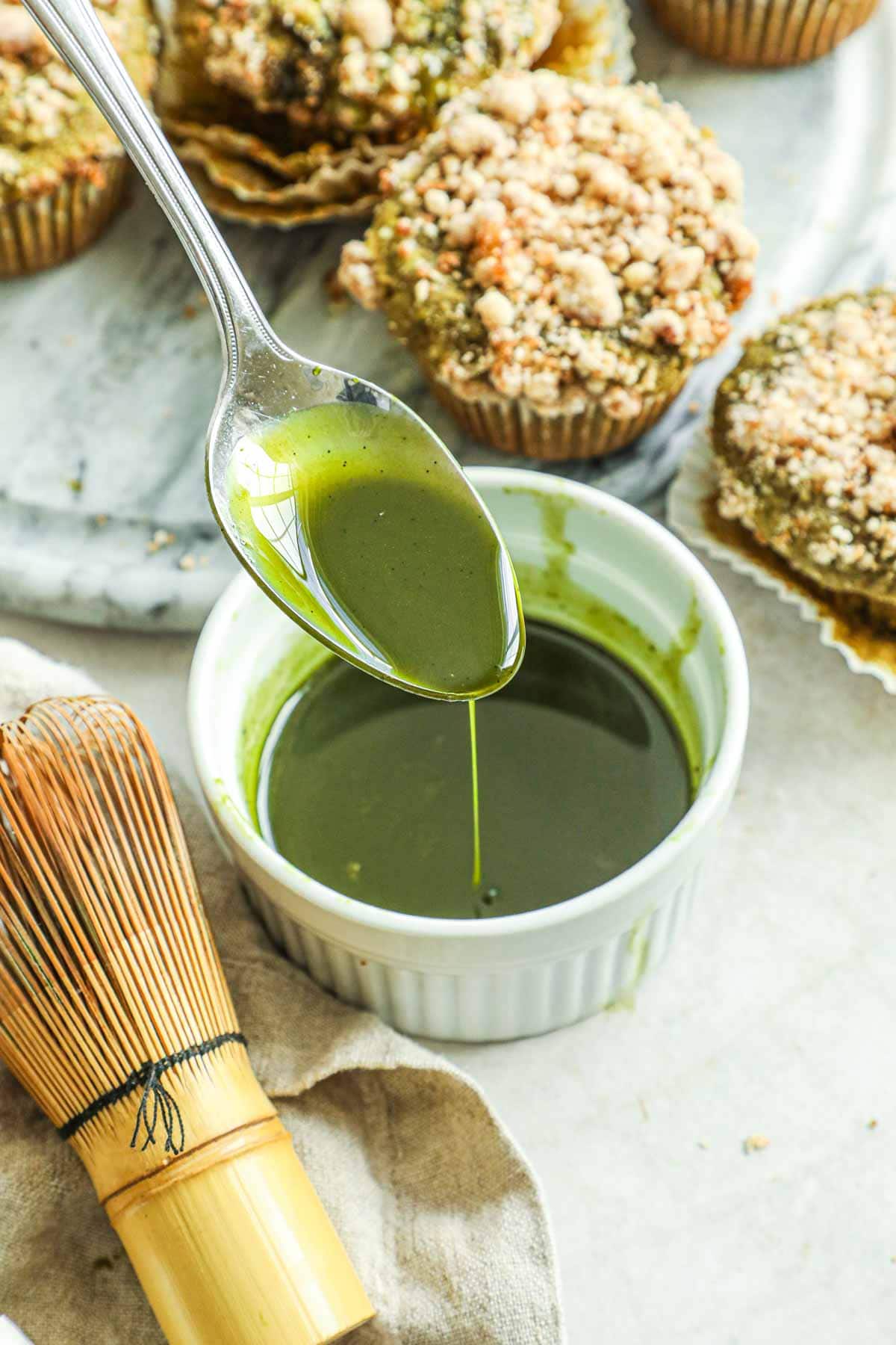 Spoon pouring matcha vanilla bean glaze for cakes, muffins, quick breads, and more in a white ceramic ramekin.