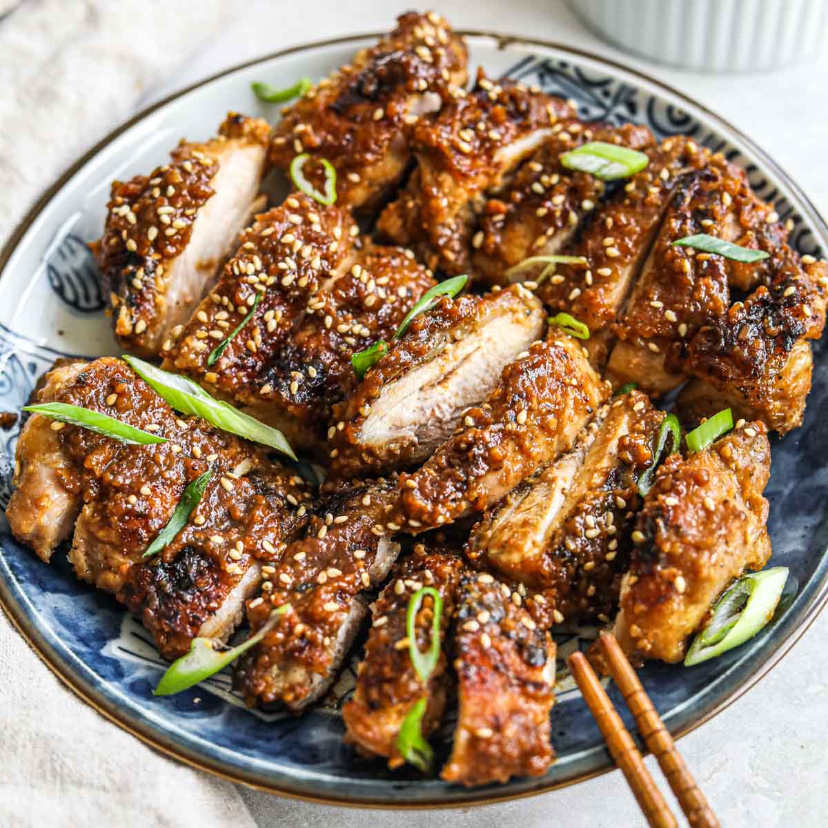 Miso jidori chicken thighs topped with sesame seeds and sliced green onions on a blue ceramic Japanese plate.