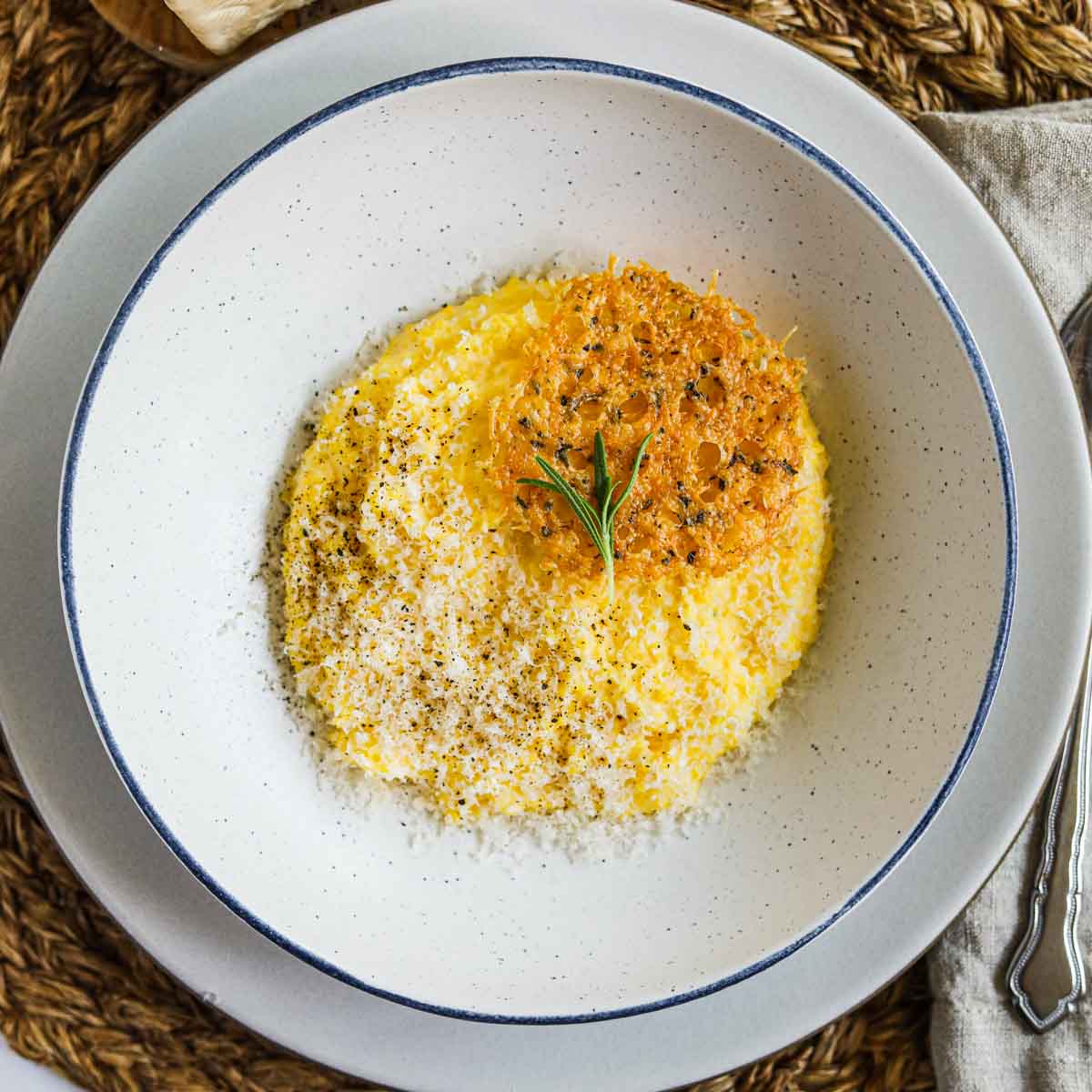 Creamy polenta with parmigiano-reggiano, rosemary, and frico (montasio cheese crisps) in a bowl.