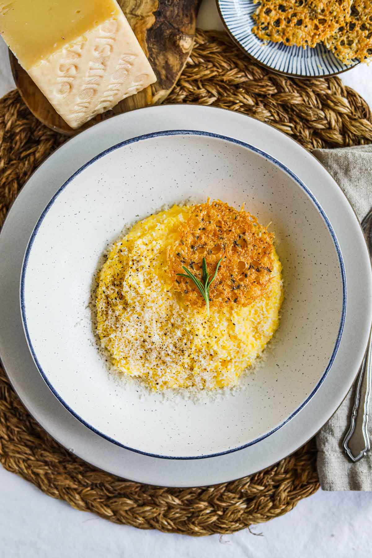 Creamy polenta with parmigiano-reggiano, rosemary, and frico (montasio cheese crisps) in a bowl.