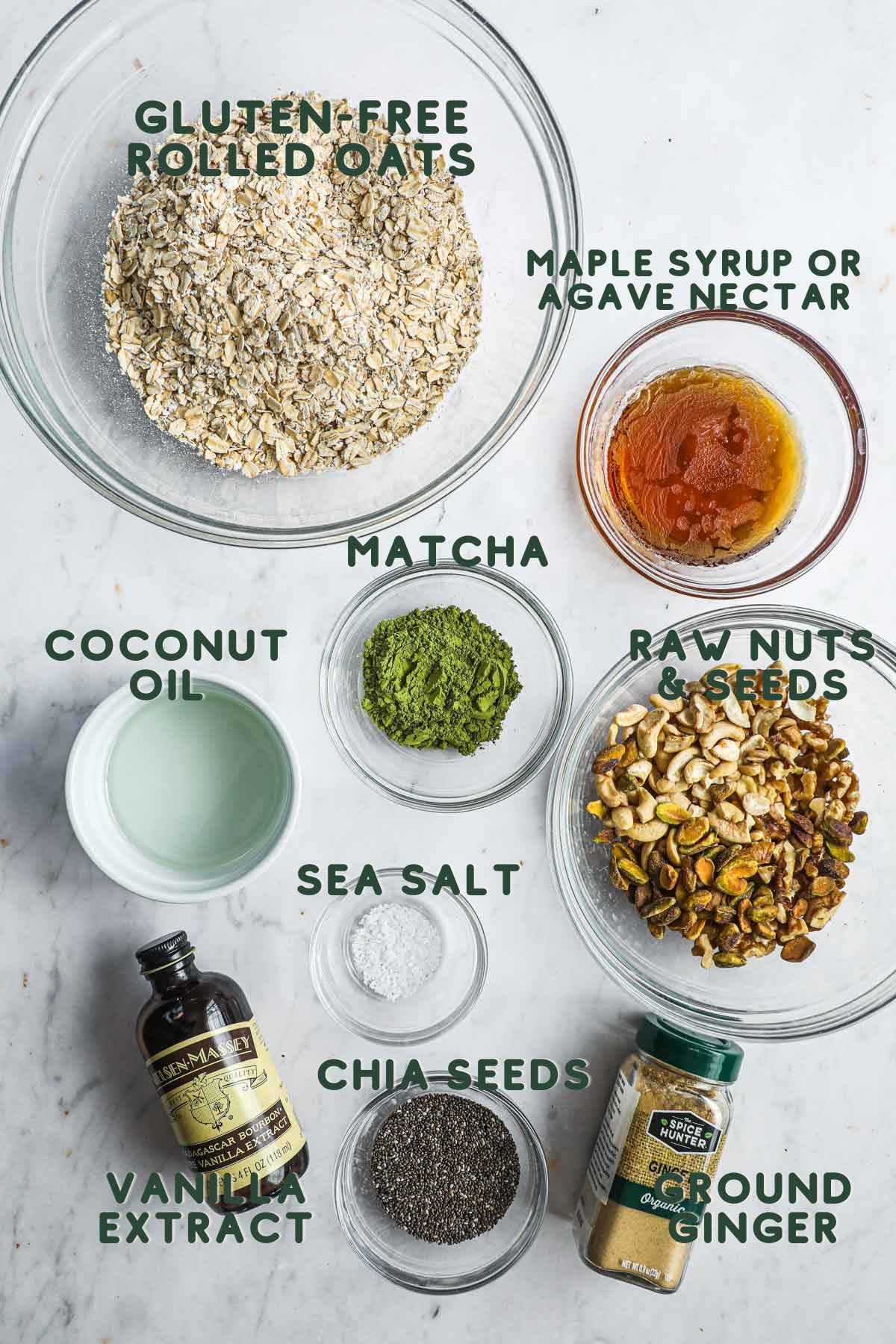 Ingredients to make gluten-free matcha granola, including rolled oats, maple syrup, seeds and nuts, coconut oil, vanilla extract, chia seeds, ground ginger, and matcha powder.