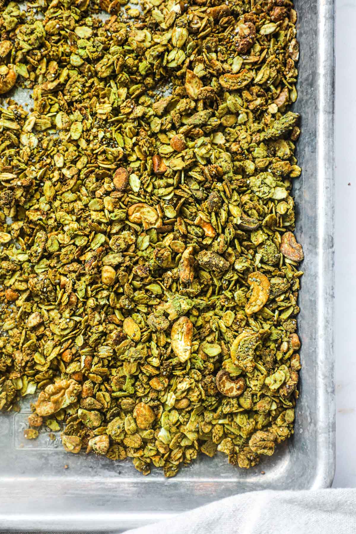 Baking sheet with green tea gluten-free matcha granola with rolled oats, seeds, and nuts.