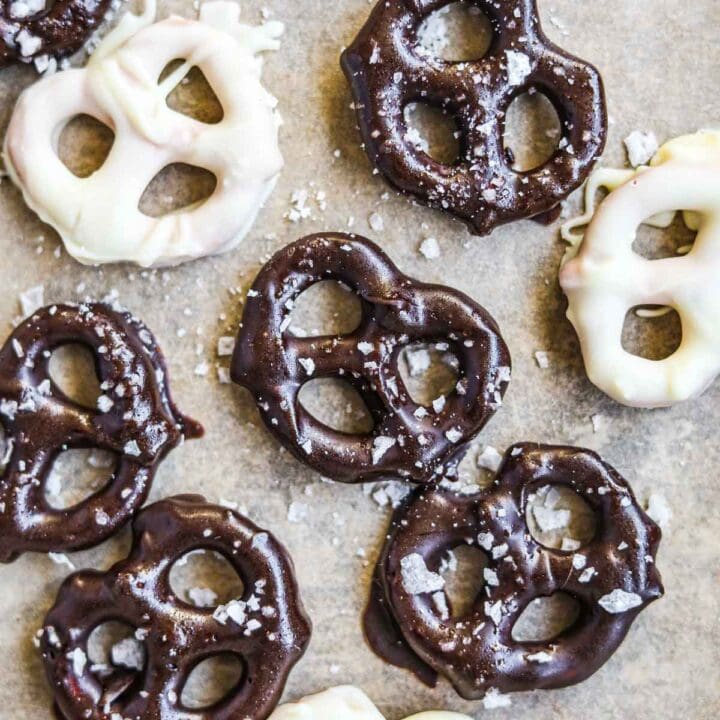 White and semi-sweet chocolate-covered pretzels with flaky sea salt on a sheet of parchment paper.