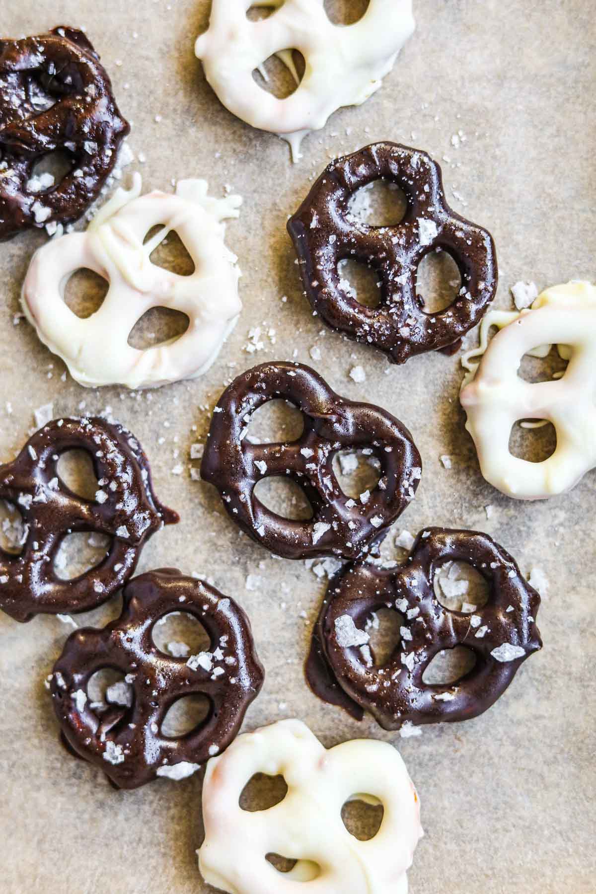 White and semi-sweet chocolate-covered pretzels with flaky sea salt on a sheet of parchment paper.