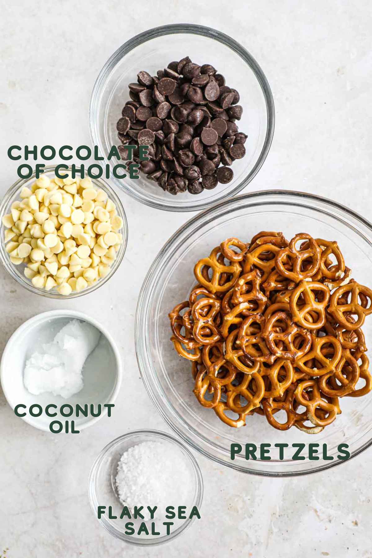 Ingredients to make chocolate-covered pretzels, including white or semi-sweet chocolate, coconut oil, flaky sea salt, and pretzels.