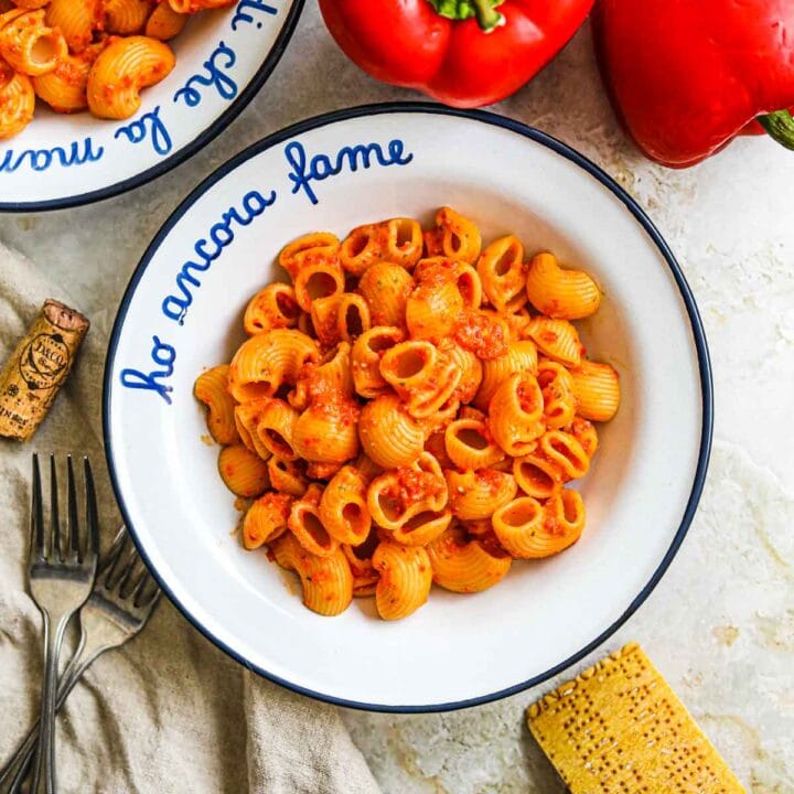 Roasted red pepper pesto pasta in a bowl with roasted red bell pepper and parmigiano-reggiano.